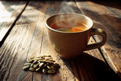 Bariatric pumpkin seed tea in a glass mug with cumin, fennel, ajwain, and pumpkin seeds on a wooden table.